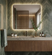 Espejo rectangular CLEOME EXPRESS con esquinas redondeadas y luz LED retroiluminada en un baño de mármol verde con mueble de madera