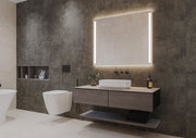 Espejo de baño rectangular HERA encendido, con luz frontal en dos franjas laterales y luz ambiental arriba y abajo, sobre un mueble de madera